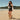 Woman in black shorts and top standing on a sandy beach wearing black Archies flip flops