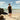 Person wearing white Archies flip flops standing on a beach with ocean and sky in the background