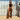Woman in black top and brown pants wearing taupe Archies flip flops standing against a white fence.