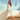 Woman in a white dress wearing orange rchies flip flops sitting on a  tiled wall 