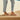 Person wearing tan Archies flip flops and light blue jeans standing on a wooden deck.