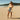 Woman wearing white Archies flip flops, denim shorts and a yellow top standing on a beach with a scenic background.